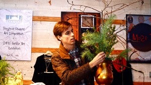 Rob Drinkard demonstrates how to arrange different floral pieces at Female Factor on Dec. 10. Drinkard gave step-by-step instructions for a carnation arrangement in stacked silver containers, a nativity scene arrangement, and a branch tree for ornaments.  MESSENGER PHOTO/COURTNEY PATTERSON