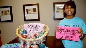 Ashlan McCloud stands a basket filled with a variety of candy apple flavors McCloud makes herself. McCloud also sells tshirts to benefit her charity, which say “Ashlan’s Awesome Apples.” This year, Ashlan plans to donate her sells to the March of Dimes.  MESSENGER PHOTO/NGOC VO