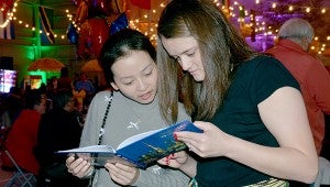 Missionaries from all over the world came to First Baptist Church’s Taste of Missions at the Global Impact Celebration. Each missionary could dress in the attire from the country they serve in while serving food from that culture. Manru Zhang, left, and Jordan Fleming read a book about Shanghai at the event.  MESSENGER PHOTO/COURTNEY PATTERSON