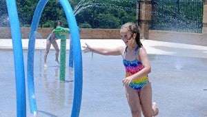 With the heat index at inching closer to 100 degrees, families are heading to the Troy Parks and Recreation Center to cool off in the water. Several families gathered at the pool Friday afternoon and enjoyed the refreshing water and spent some time playing on the Splash Pad. Emma Marlow, front, runs away as her sister, Mary Eden, sprays her with a water gun in the Splash Pad.  MESSENGER PHOTO/COURTNEY PATTERSON
