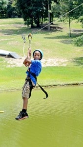 MESSENGER PHOTO/COURTNEY PATTERSON The Boys and Girls Club took on new adventures at Camp Butter and Egg Friday. Jimaryon Lykes rides a zip line over the lake.