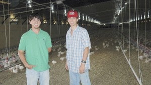 MESSENGER PHOTO/JAINE TREADWELL Halston Motes, left, and his friend, Austin Adler stand in a chicken house with about a football field’s length worth of chickens behind them