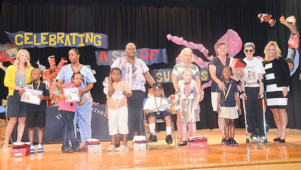 Eight Troy Elementary School students are Achilles Kids. To achieve the award, each kid had to walk, run, skip, hop or ride a tricycle or scooter 26.2 miles. Pictured with their Achilles Kids certificates and prizes are, from left, Jalen Robinson, Alina Pressley, Joshua Powell, Desiree Love, Madysin Green and Janiya Crosky. Not pictured, Raqual Cooper and Wyatt Taylor. Also pictured, Dana Haley, Kids teacher, center; and Achilles Kids Director Karen Lewis and Dr. Candy Shaughnessy, Troy University, far right. Below, high 5’s exchanged between Karen Lewis, Achilles Kids director, Joshua Powell, as Dr. Candy Shaughnessy watches.